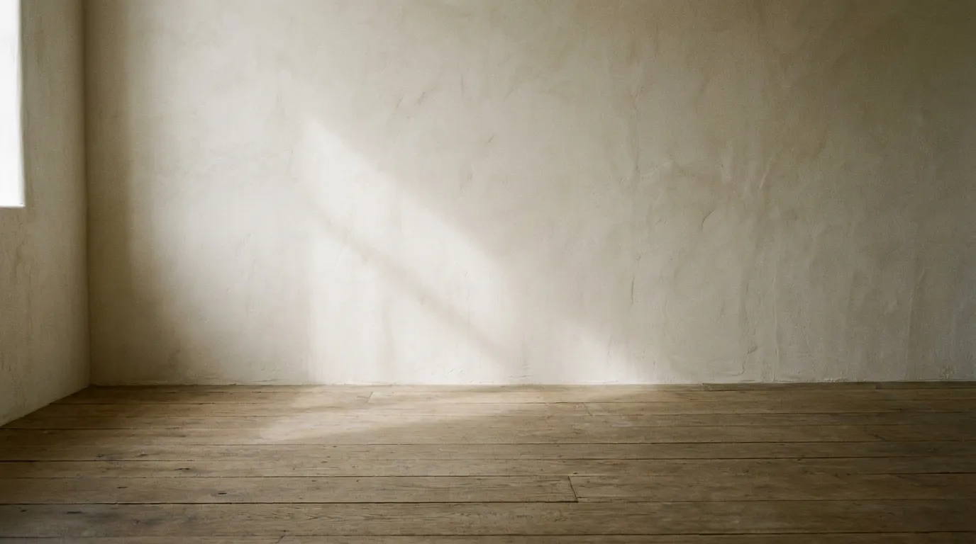 An empty room corner where plaster wall meets oak floor